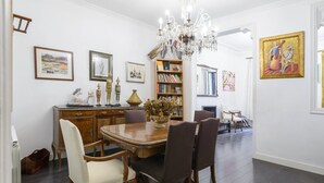 Uma sala de jantar com uma mesa de madeira, cadeiras, um candelabro e uma estante repleta de livros.