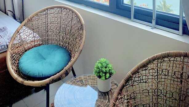 A balcony with wicker chairs, a small table, and a view of the sea with boats. - Gem Hostel (Hai Phong)