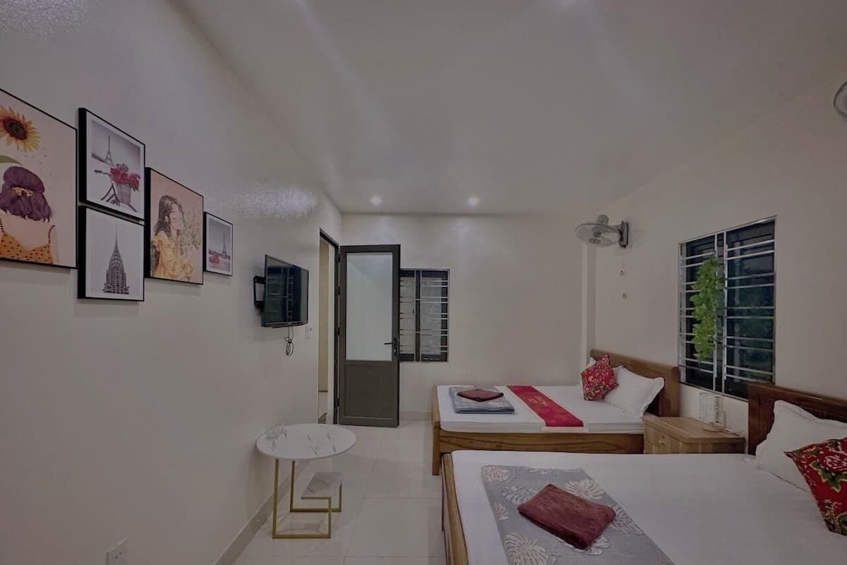 A hotel room with two beds, a small table, a TV, and framed artwork on the walls.