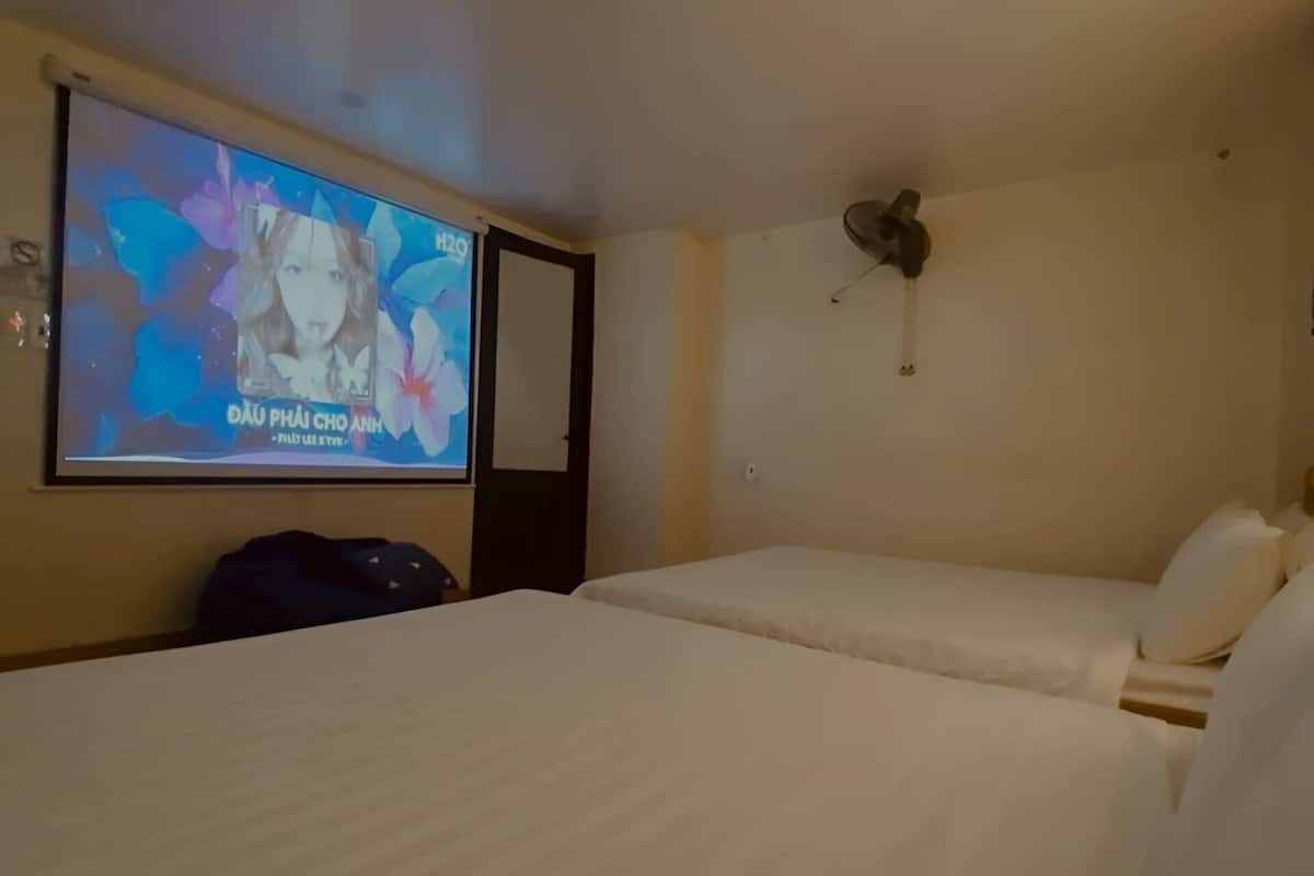 A hotel room with two beds, a television on the wall, and a ceiling fan.