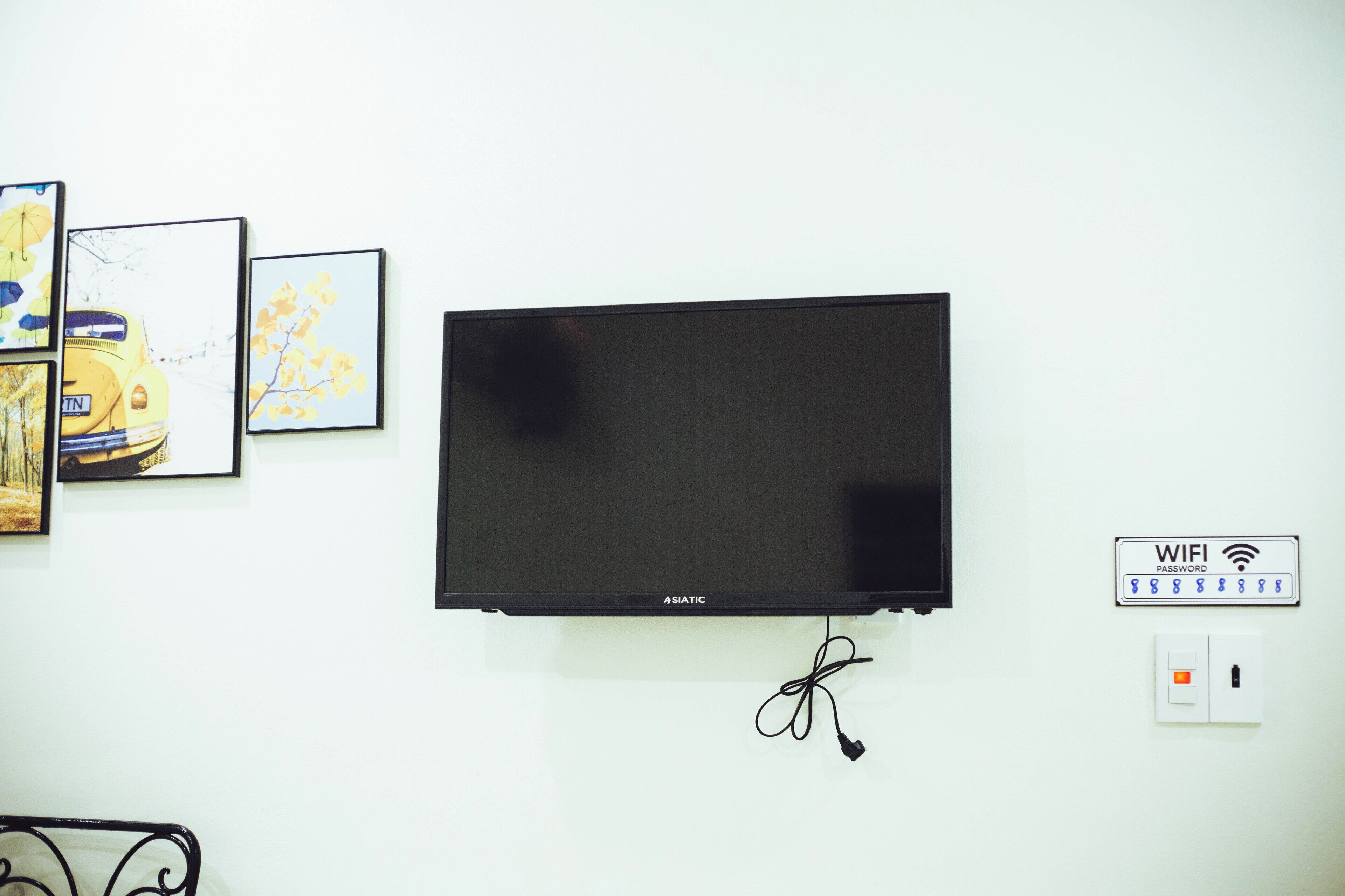 A flat-screen TV mounted on a white wall, with a power cord and a WiFi password sign nearby.