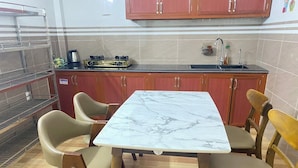 A dining area with a marble table and wooden chairs, a kitchen with red cabinets and a gas stove, and a tiled backsplash. - Gem Hostel (Hai Phong)