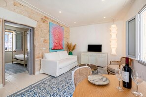 Un salon moderne avec un canapé blanc, une table à manger avec des chaises, un téléviseur et une bouteille de vin.
