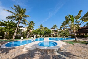A resort pool area with multiple swimming pools, palm trees, and a clear blue sky.