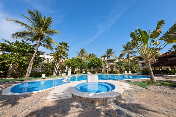 A resort pool area with multiple swimming pools, palm trees, and a clear blue sky.