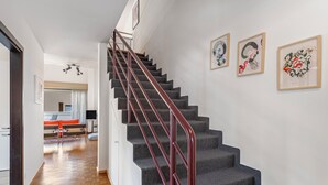 Una escalera con barandilla roja que sube a un segundo piso. Encima de las escaleras, hay tres obras de arte enmarcadas en la pared.