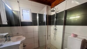 Ein kleines Badezimmer mit Duschkabine aus Glas, einem weißen Waschbecken und einer Toilette.