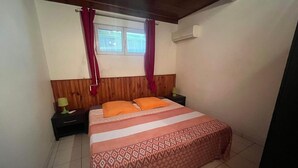 Ein Schlafzimmer mit einem Bett, zwei Nachttischen, einem Vorhangfenster und einer Klimaanlage.