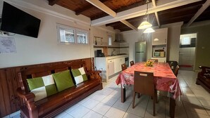 Ein gemütliches Wohnzimmer mit einem Holzdile und einem Esstisch mit Stühlen, im Hintergrund eine Küche.