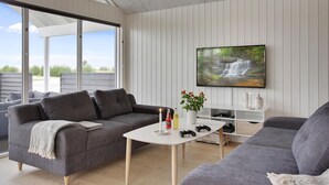 Una sala de estar moderna con un sofá gris, una mesa de centro y un televisor en la pared que muestra una escena de cascada.