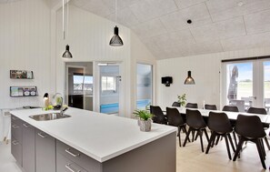 Une cuisine moderne dotée d’un grand îlot central, d’un coin repas avec des chaises et d’une vue sur l’extérieur.