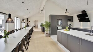Una cocina moderna con una larga mesa de comedor, electrodomésticos integrados e iluminación colgante.