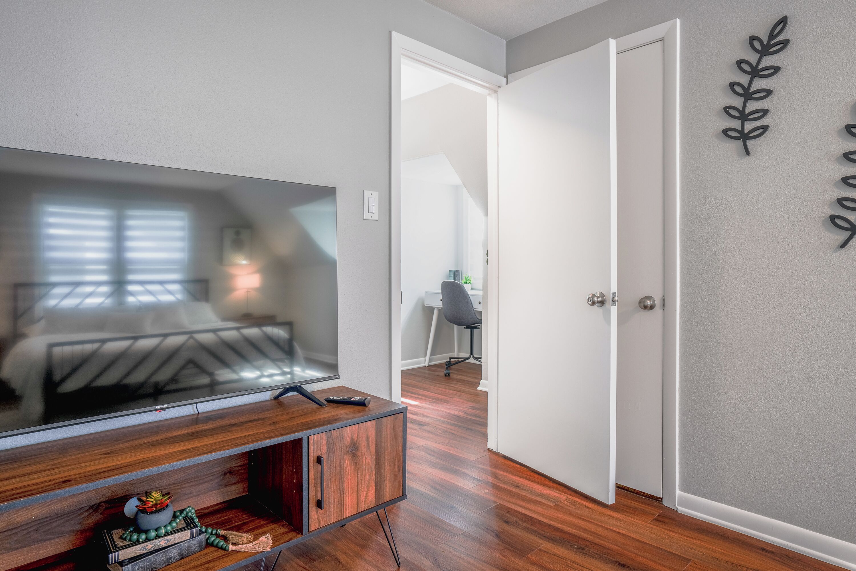 A modern living room with a flat-screen TV on a wooden console, a small plant, and a remote control.
