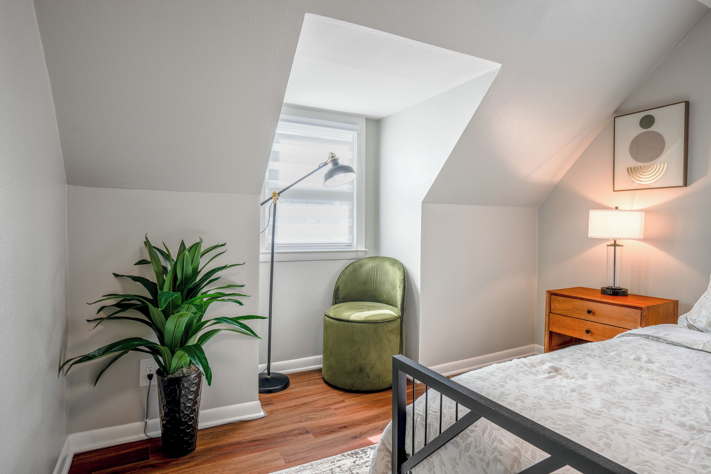 Une chambre à coucher avec un lit, un fauteuil vert, une lampe sur pied, une table de chevet et une plante en pot.