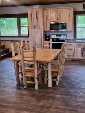 A wooden dining table with chairs, a kitchen with wooden cabinets, a microwave, and a coffee maker. - Mountain View Lodge w/ Pavilion & Fire Pit (Beaver Dams)