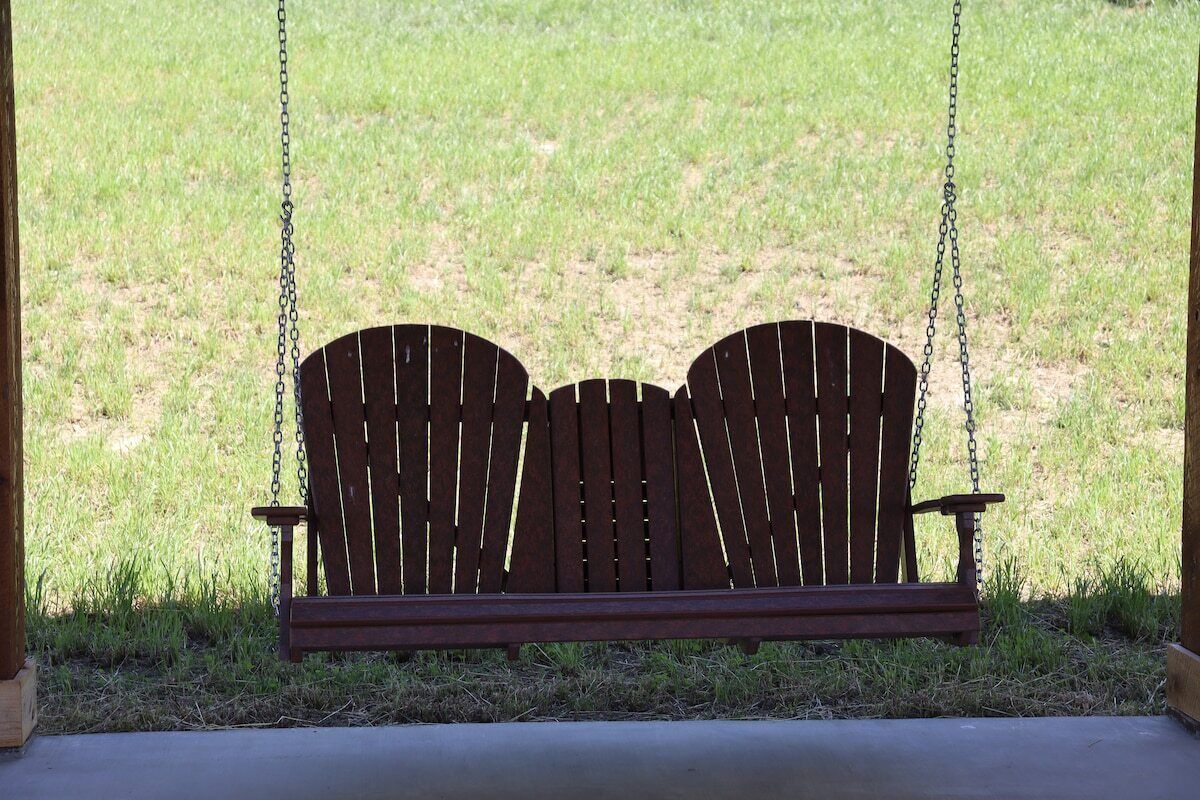 A wooden swing bench with a metal chain, set against a grassy background.