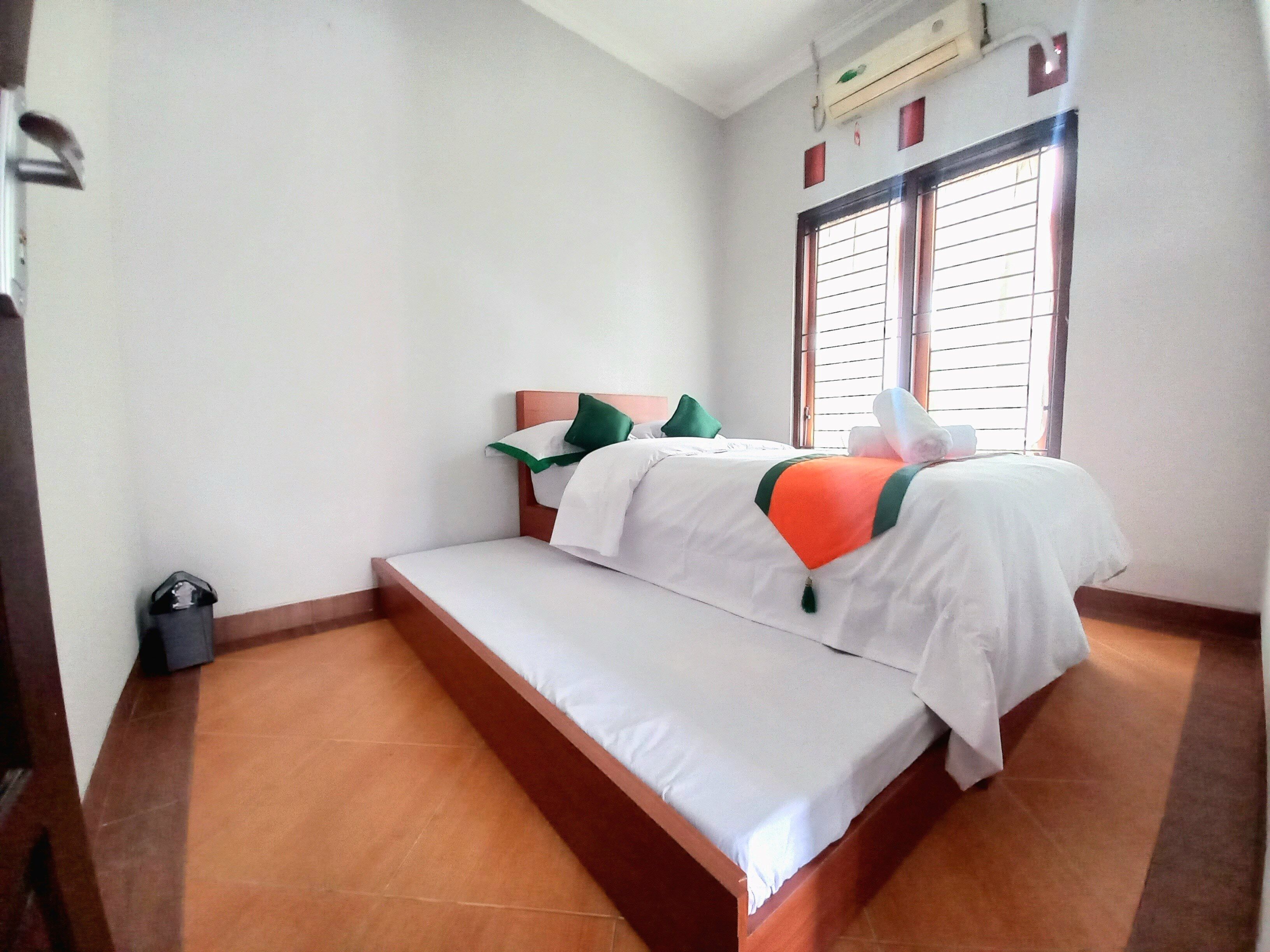 A single bed with a wooden frame, a bench, and a window with blinds.