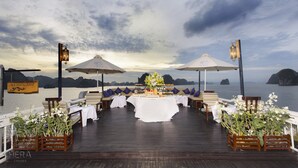 A dining area with a table set for two, overlooking a body of water with islands in the distance. - Hera Grand Luxury Cruise (Tuan Chau)