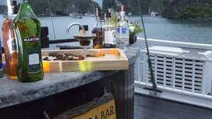 A bar with a wooden sign reading "Panthera Bar" on a boat deck with a view of the water and mountains in the background. - Hera Grand Luxury Cruise (Tuan Chau)