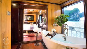 A luxurious cabin with a large bathtub, wooden flooring, a bed with a view, and a dining area. - Hera Grand Luxury Cruise (Tuan Chau)