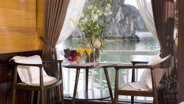 A dining area with two chairs, a table with fruit and drinks, and a view of a rocky coastline. - Hera Grand Luxury Cruise (Tuan Chau)
