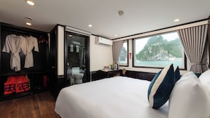 A hotel room with a large bed, a wardrobe, a bathroom, and a view of a mountainous landscape. - Amanda Cruise Ha Long Bay (Tuan Chau)
