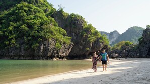 A beach with rocky cliffs and lush greenery. - Amanda Cruise Ha Long Bay (Tuan Chau)