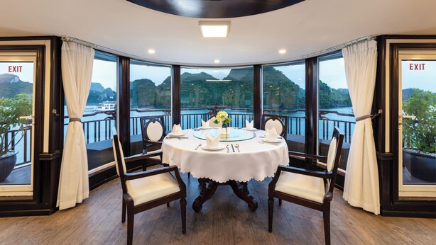 A round table with chairs in a room with large windows and an 'EXIT' sign on the walls. - Amanda Cruise Ha Long Bay (Tuan Chau)