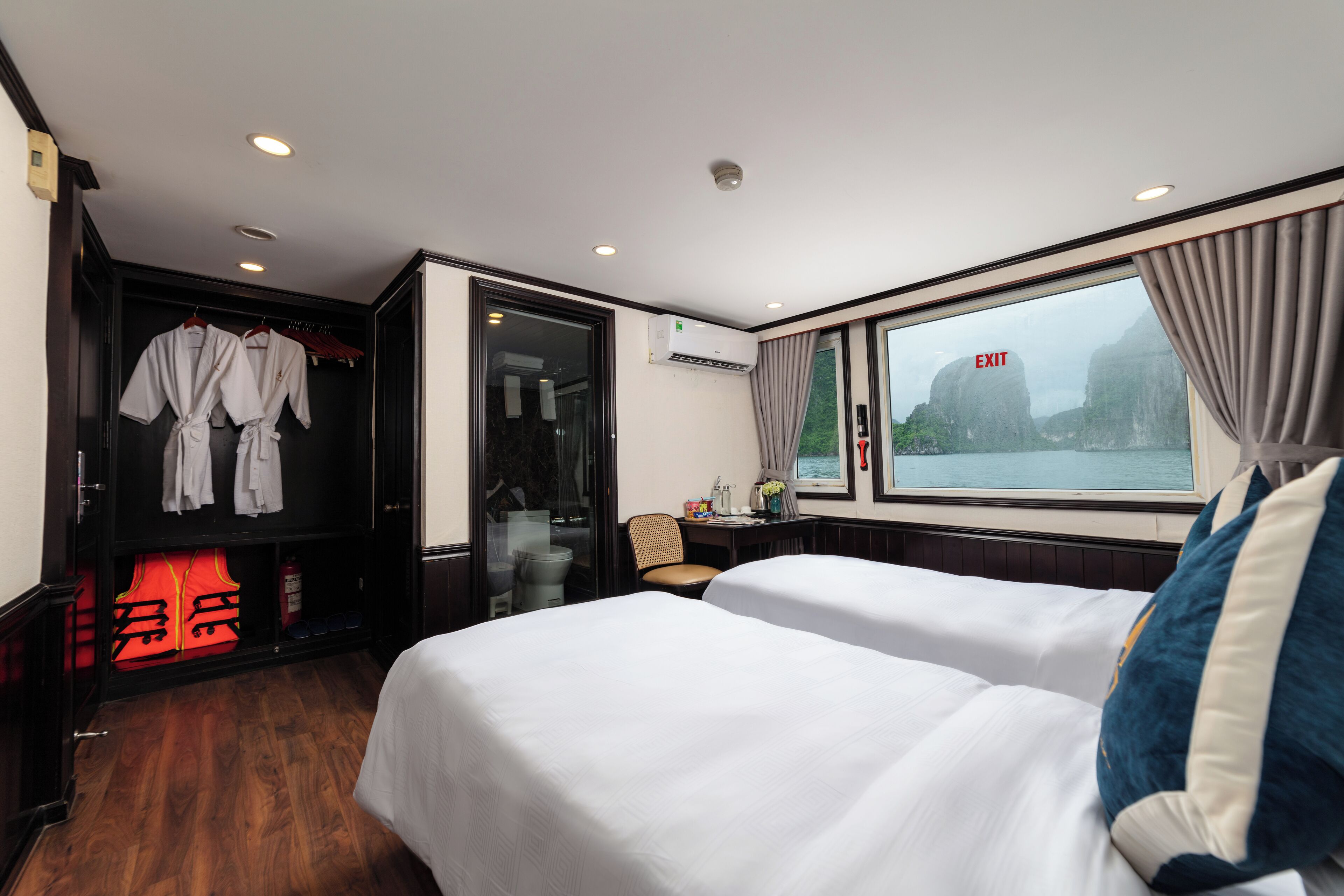 A hotel room with two beds, a wardrobe, a desk, and a window with a view of a mountain.