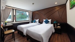 A hotel room with two beds, a desk, a chair, and a window with a view of greenery. - Amanda Cruise Ha Long Bay (Tuan Chau)