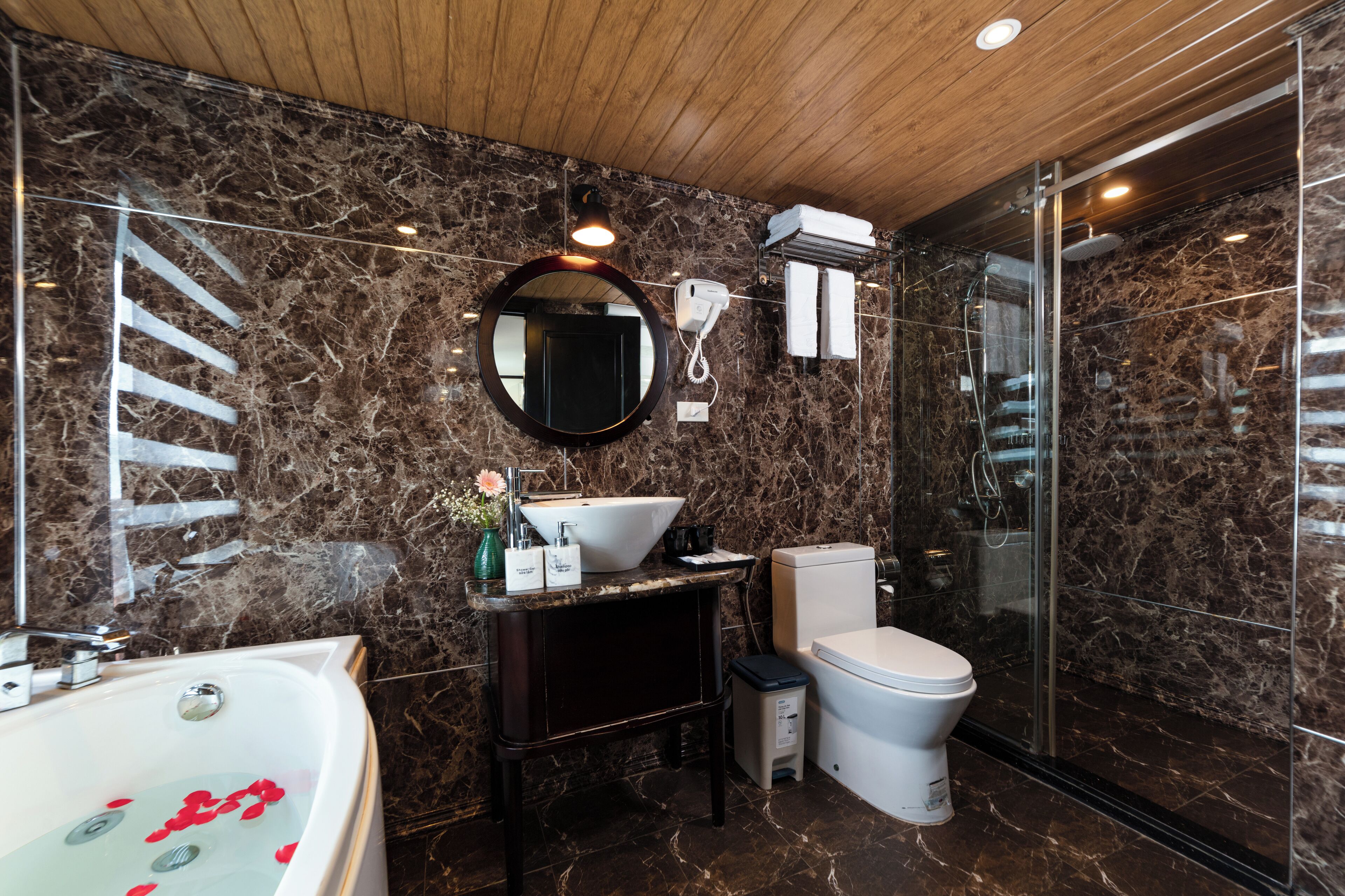 A modern bathroom with a marble wall, a round mirror, a sink, a toilet, and a glass-enclosed shower.