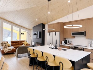 A modern kitchen with a central island, wooden cabinets, and a built-in microwave. - 4 BR with Epic Mountain View, Hot Tub, Garage EV Port, Super High Ceiling (Canmore)