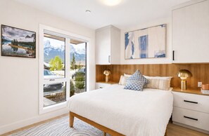Ett sovrum med en stor säng, en sänggavel i trä, sänglampor och utsikt över bergen genom en skjutdörr.