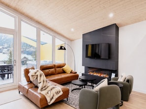 Una sala de estar moderna con chimenea, sofá de cuero y televisor montado en la pared.