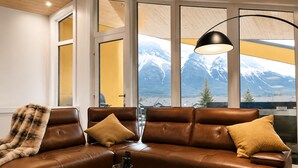 A brown leather sofa with cushions, a round coffee table, and a pendant lamp. - 4 BR with Epic Mountain View, Hot Tub, Garage EV Port, Super High Ceiling (Canmore)