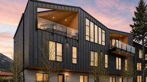 A modern multi-story building with large windows, balconies, and a stone facade. - 4 BR with Epic Mountain View, Hot Tub, Garage EV Port, Super High Ceiling (Canmore)