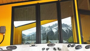 A hot tub with a view of snow-capped mountains through large windows. - 4 BR with Epic Mountain View, Hot Tub, Garage EV Port, Super High Ceiling (Canmore)