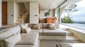 A modern living room with a large sectional sofa, a staircase, and a view of the ocean.