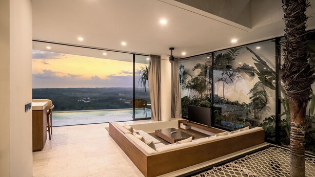 A modern bedroom with a large bed, a TV, and a view of a sunset over a body of water.