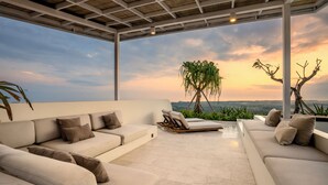 A modern outdoor lounge area with a white sofa and lounge chairs, a pergola, and a view of the landscape.