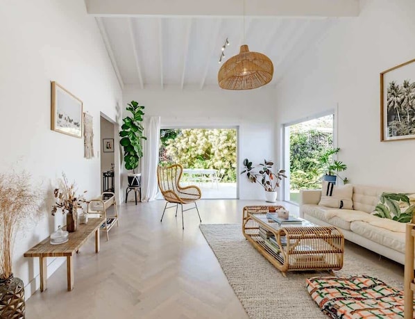 A spacious living room with a high ceiling, a large window, and a view of greenery outside.