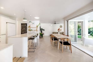 A modern kitchen with bar stools, a dining area with a table and chairs, and a large sliding glass door leading to a garden.