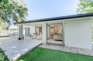 A modern house with a covered patio, a glass door leading to a living room, and a well-maintained lawn.