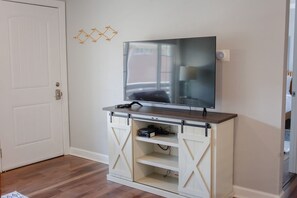 Una habitación con televisor sobre un soporte de madera, una puerta con cerradura y un interruptor de luz fijado a la pared.