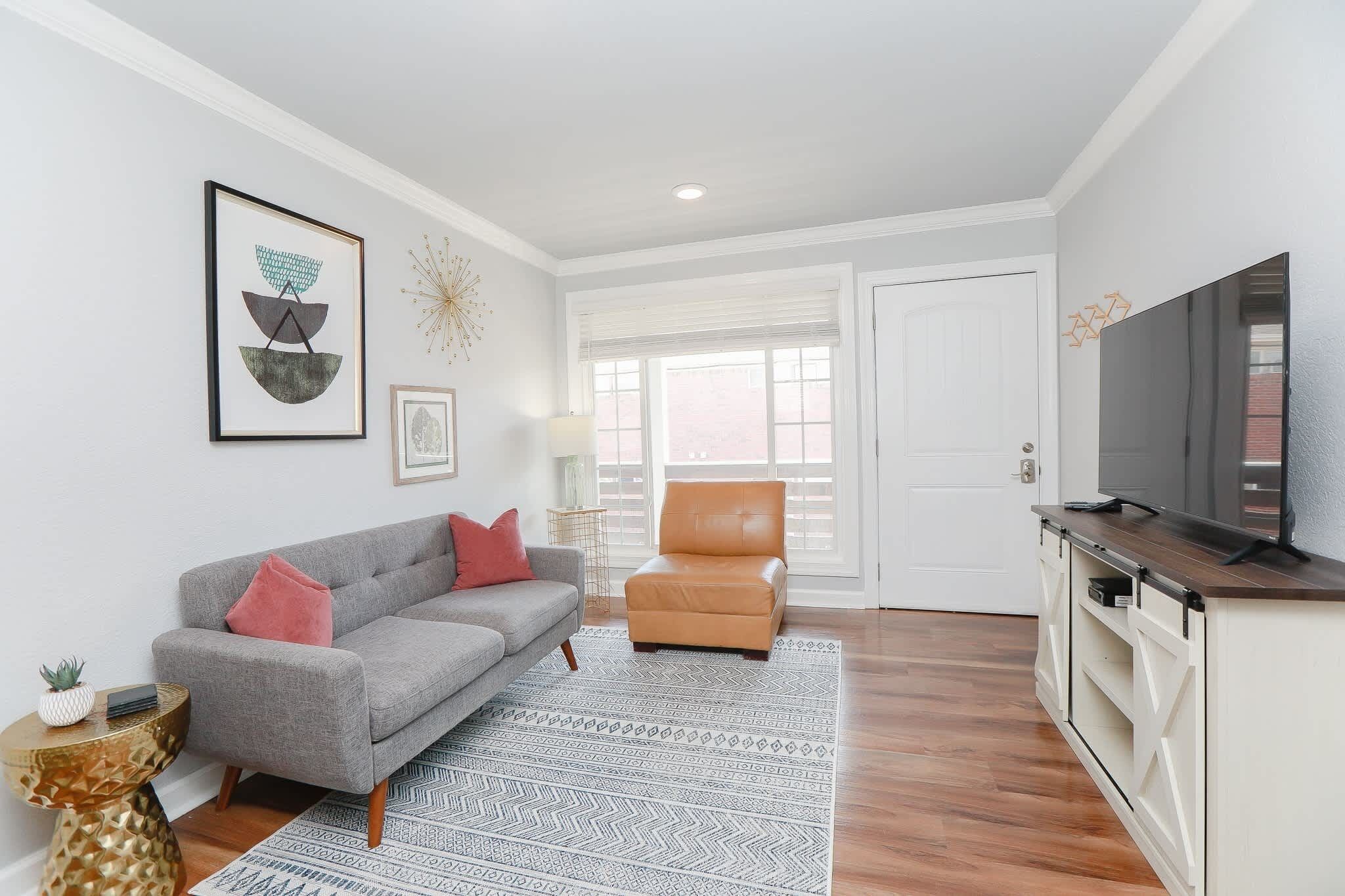 A modern living room with a grey sofa, a brown armchair, a flat-screen TV, and a patterned rug.