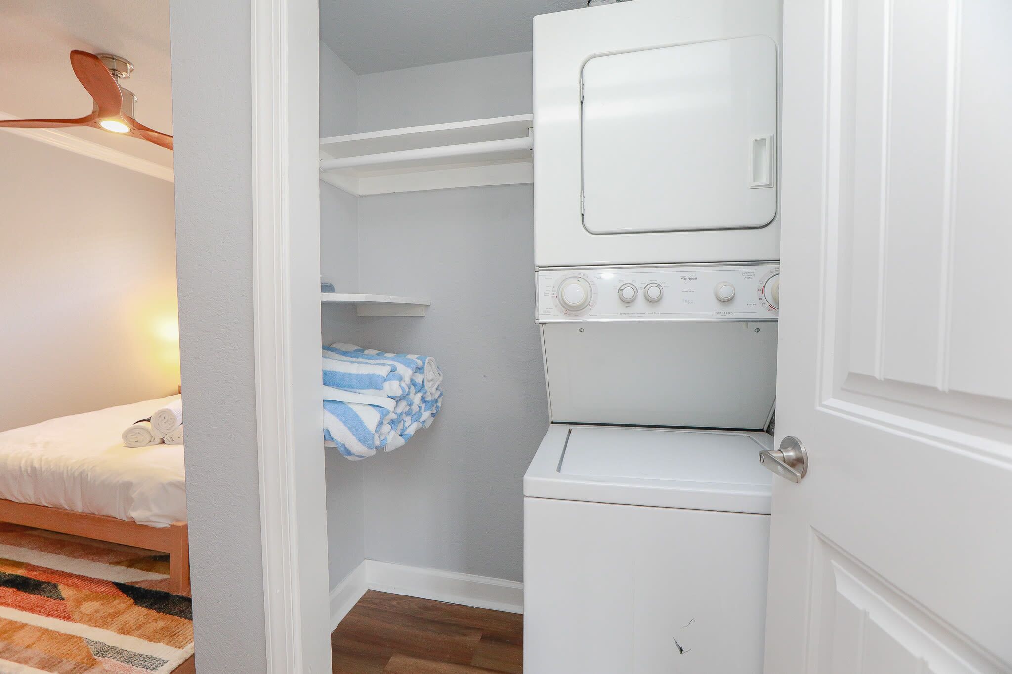 A laundry room with a stacked washer and dryer, a bed with rolled towels, and a patterned rug.