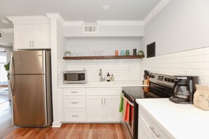 A modern kitchen with white cabinetry, a stainless steel refrigerator, a microwave, a stove, and a coffee maker.