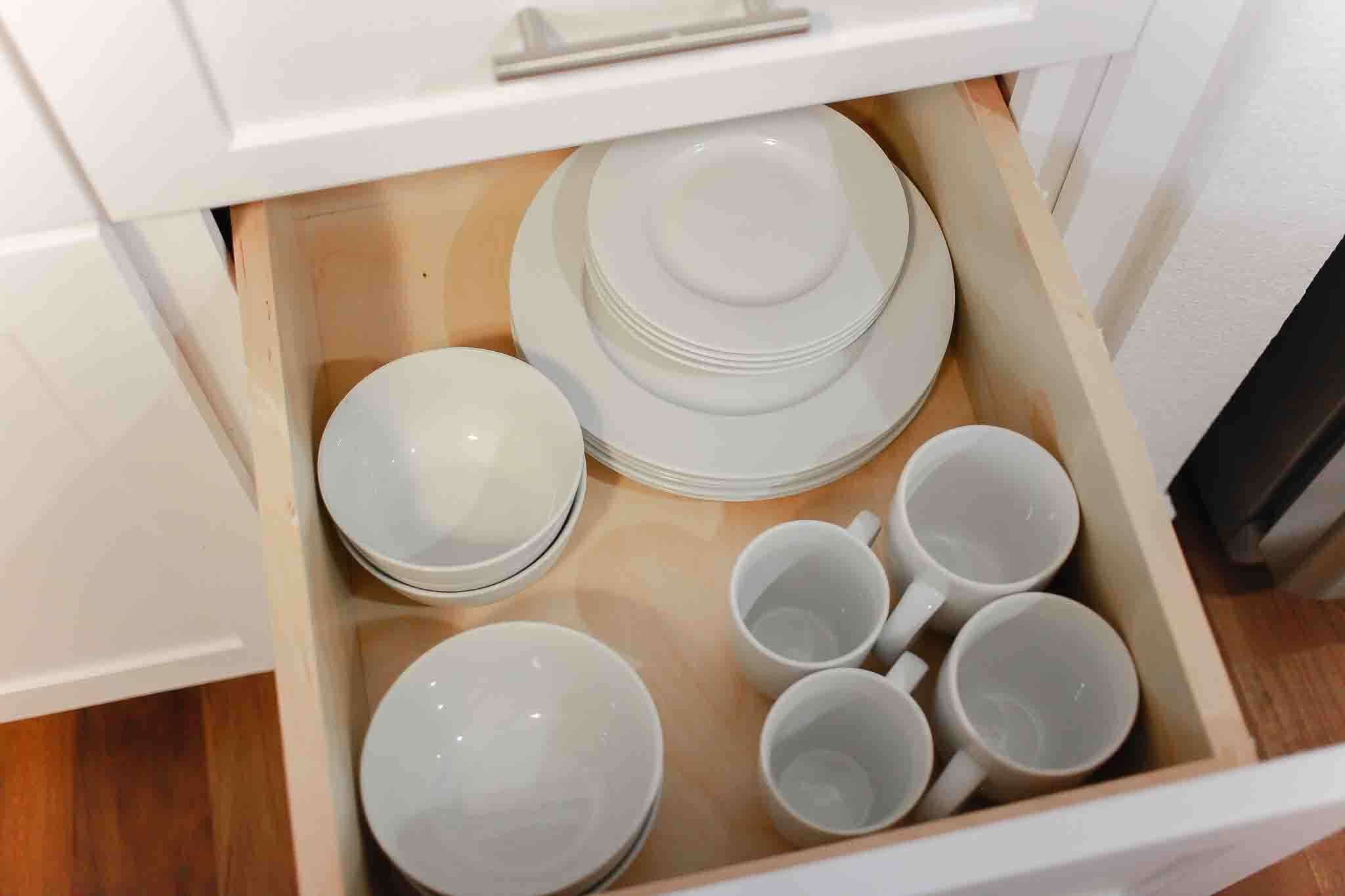 A drawer containing white plates and cups.