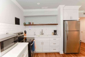 A modern kitchen with white cabinetry, a stainless steel refrigerator, and a built-in oven. - Sojourn Salt Suite 2 BR 2 BA at Beach Cottages (Norfolk)