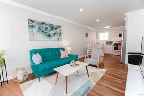 Una sala de estar moderna con un sofá color turquesa, una mesa de centro blanca y una cocina al fondo.